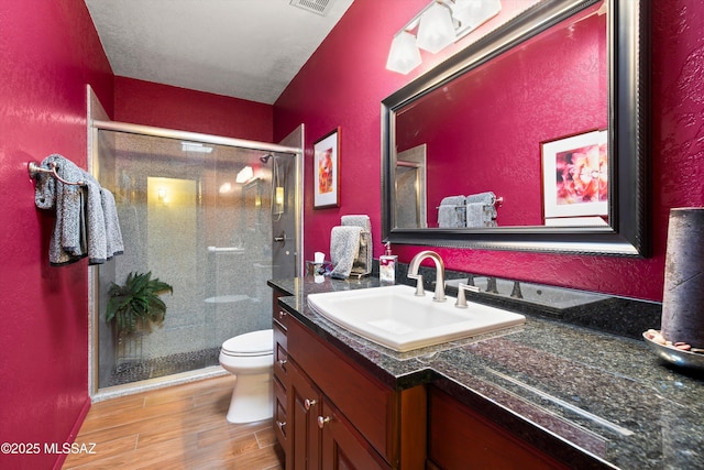 bathroom with visible vents, toilet, wood finished floors, a shower stall, and vanity