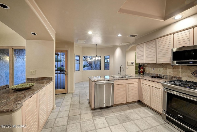 kitchen with stainless steel appliances, a peninsula, a sink, visible vents, and tasteful backsplash