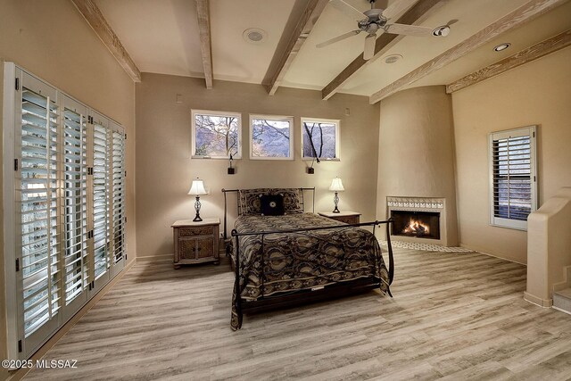 bedroom with a large fireplace, multiple windows, beamed ceiling, and wood finished floors