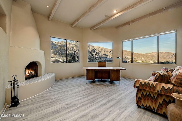 office space featuring light wood-type flooring, a large fireplace, baseboards, and beam ceiling