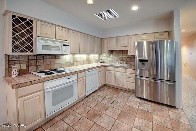 kitchen featuring white appliances, a sink, visible vents, backsplash, and tile counters