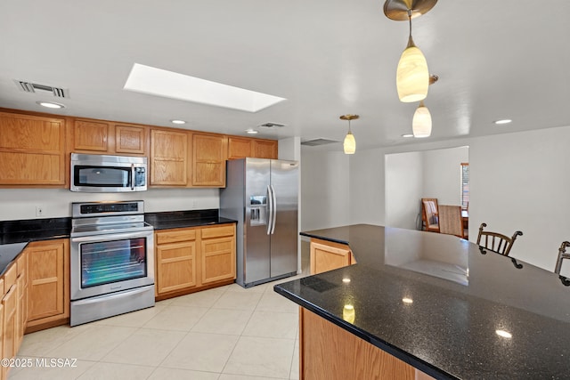 kitchen featuring a skylight, decorative light fixtures, dark stone counters, light tile patterned floors, and stainless steel appliances