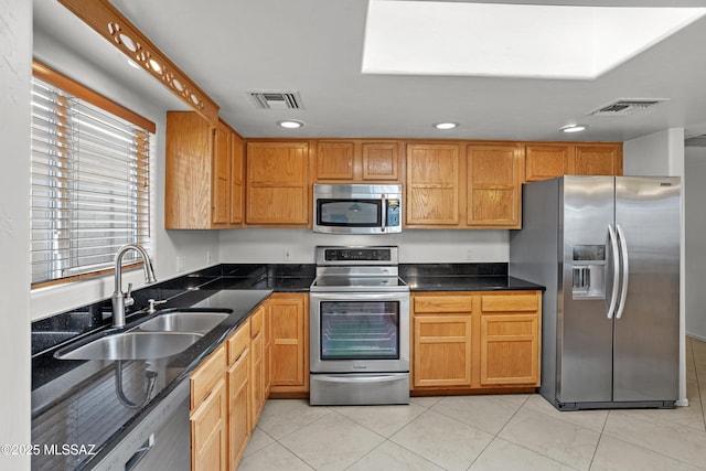 kitchen with sink, light tile patterned floors, dark stone counters, and appliances with stainless steel finishes