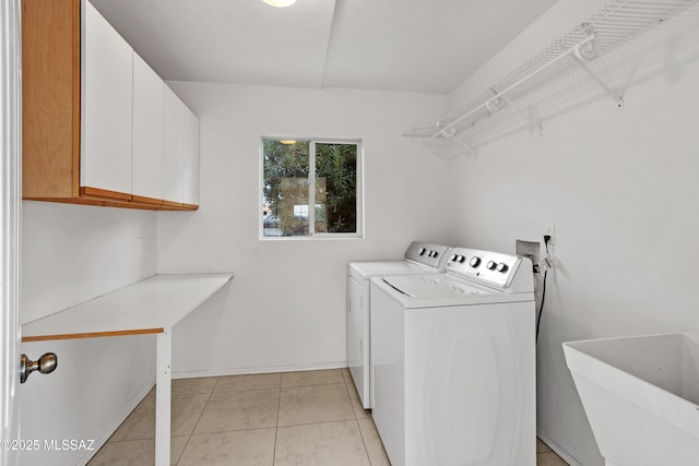 clothes washing area with sink, light tile patterned floors, washing machine and dryer, and cabinets