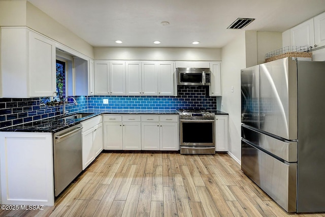 kitchen with a sink, visible vents, appliances with stainless steel finishes, light wood finished floors, and tasteful backsplash