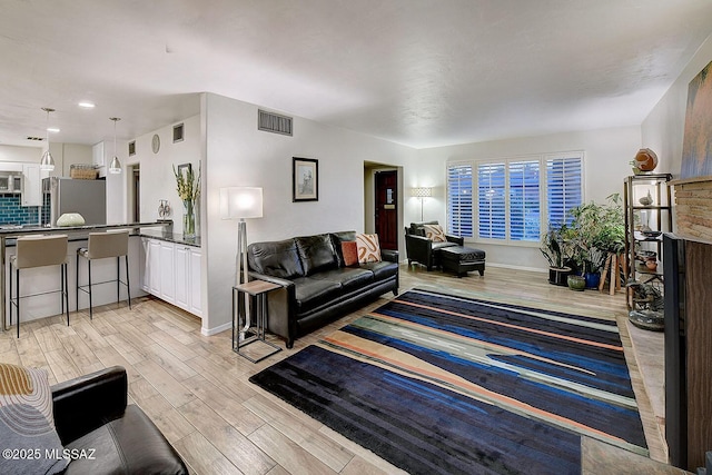 living area featuring baseboards, visible vents, and light wood finished floors