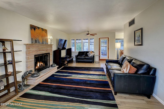 living room with light wood finished floors, baseboards, visible vents, a ceiling fan, and a fireplace