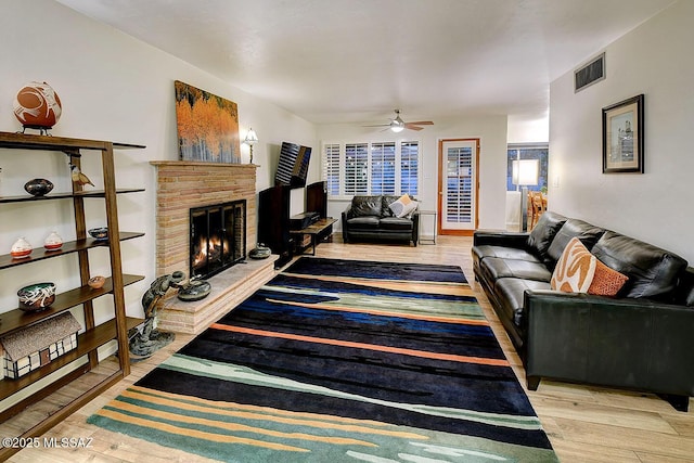 living room featuring a ceiling fan, visible vents, a fireplace, and wood finished floors