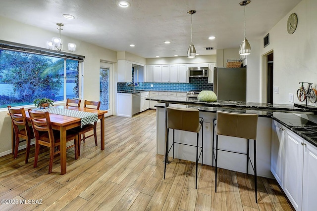 kitchen with light wood-style flooring, decorative backsplash, appliances with stainless steel finishes, white cabinets, and a kitchen breakfast bar