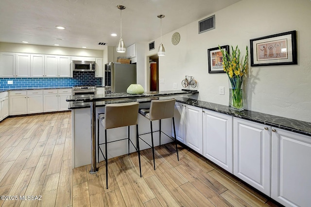 kitchen featuring visible vents, appliances with stainless steel finishes, light wood-type flooring, white cabinetry, and backsplash