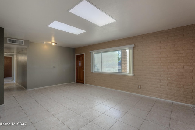 unfurnished room featuring light tile patterned flooring, brick wall, and a skylight