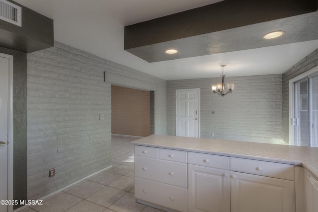 kitchen featuring brick wall, white cabinets, a chandelier, hanging light fixtures, and light tile patterned floors