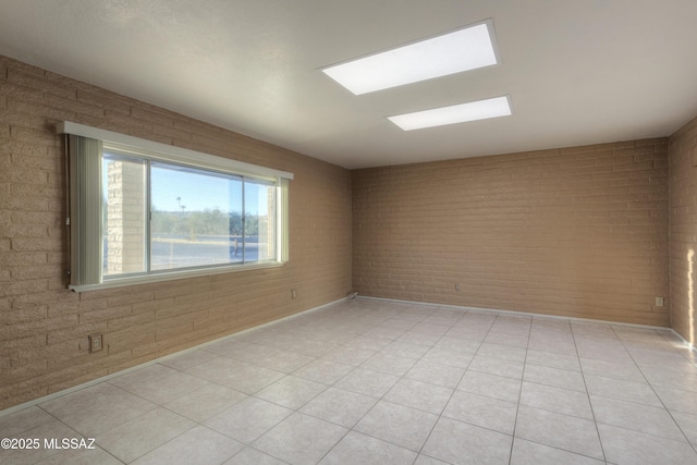 unfurnished room featuring brick wall, light tile patterned floors, and a skylight