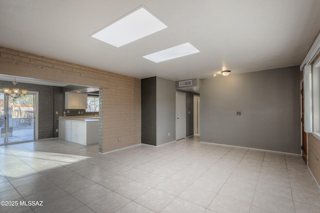 unfurnished living room with an inviting chandelier, a skylight, brick wall, and light tile patterned flooring