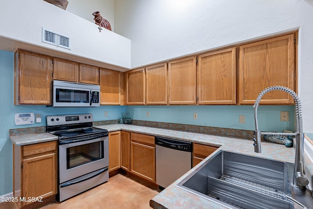 kitchen with stainless steel appliances, sink, light tile patterned floors, and a towering ceiling