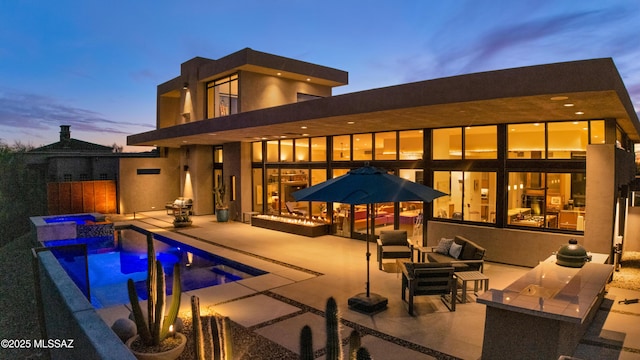 back of property at dusk with an outdoor pool, outdoor lounge area, a patio, and an in ground hot tub