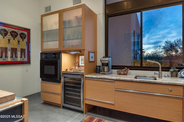 kitchen with beverage cooler, visible vents, glass insert cabinets, oven, and a sink