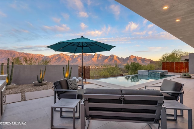 patio terrace at dusk with a pool with connected hot tub, a fenced backyard, a mountain view, and an outdoor living space