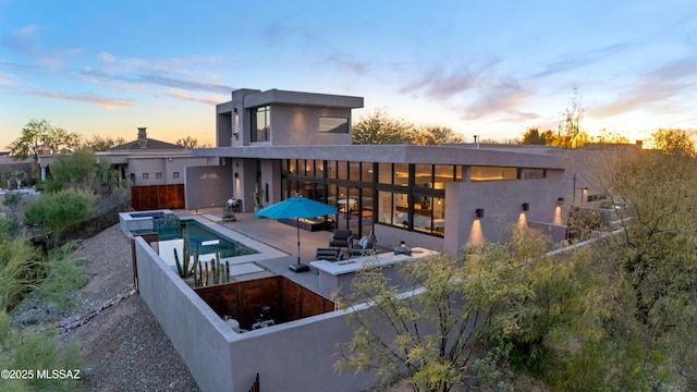 back of property at dusk with a patio area, an outdoor pool, and fence