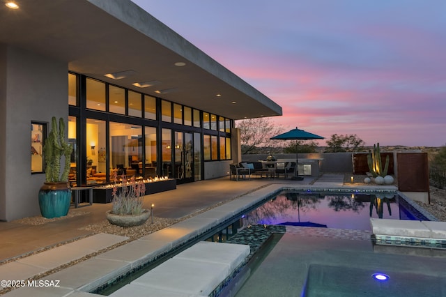 pool at dusk with a pool with connected hot tub and a patio