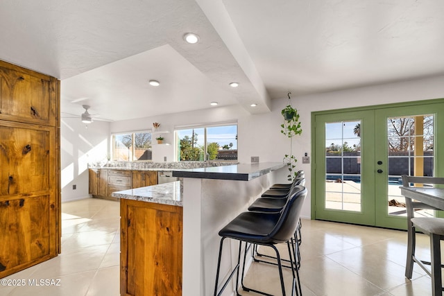 kitchen featuring a breakfast bar, stainless steel dishwasher, light tile patterned floors, kitchen peninsula, and french doors