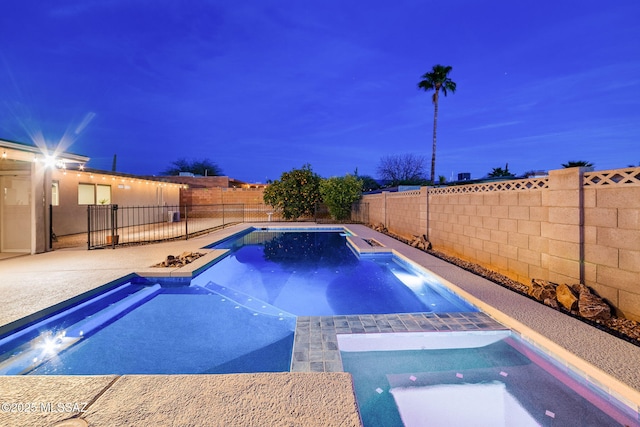 pool at dusk featuring a patio area and an in ground hot tub