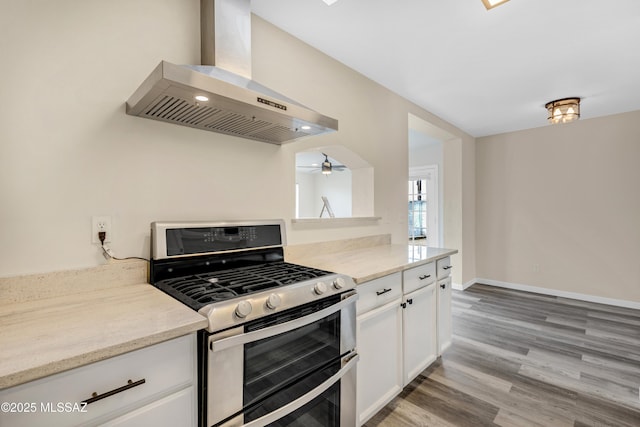 kitchen featuring double oven range, ventilation hood, light hardwood / wood-style floors, light stone countertops, and white cabinets