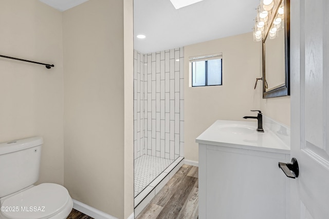 bathroom with a tile shower, vanity, wood-type flooring, and toilet