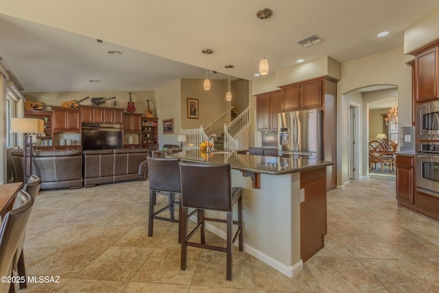 kitchen with a breakfast bar, dark stone countertops, a kitchen island with sink, stainless steel appliances, and decorative light fixtures