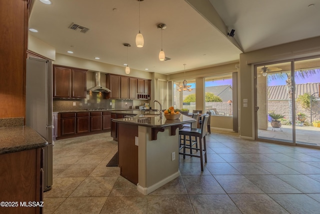 kitchen with a kitchen bar, hanging light fixtures, wall chimney range hood, stainless steel appliances, and backsplash