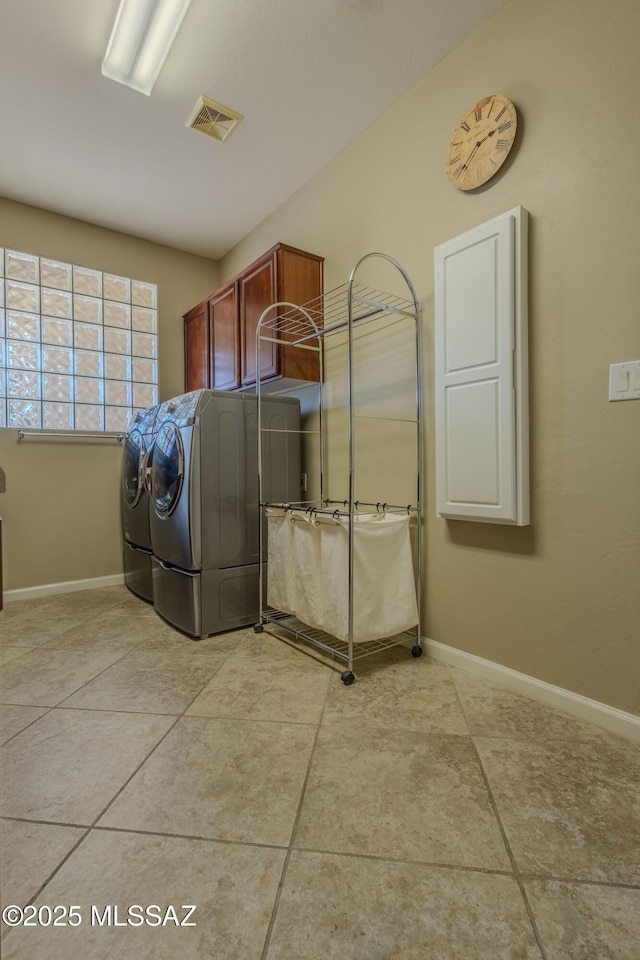 clothes washing area with cabinets, light tile patterned floors, and washing machine and clothes dryer