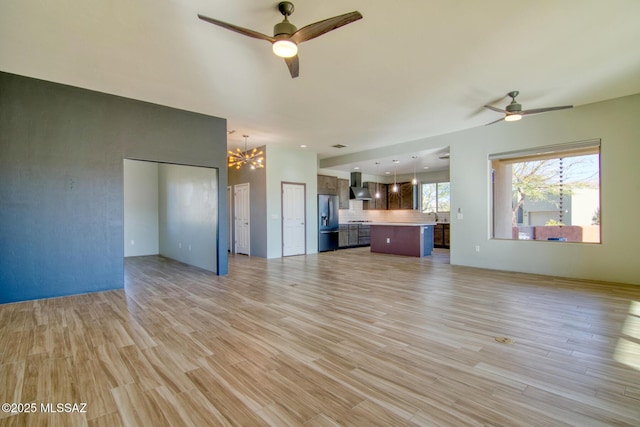 unfurnished living room featuring ceiling fan with notable chandelier and light wood-type flooring