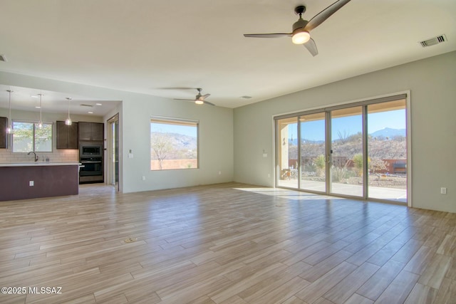 unfurnished living room with a mountain view, a wealth of natural light, sink, and ceiling fan