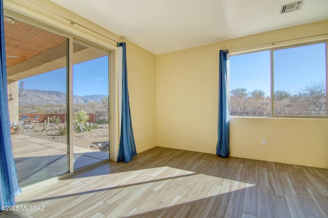 unfurnished room with a mountain view, a healthy amount of sunlight, and light wood-type flooring