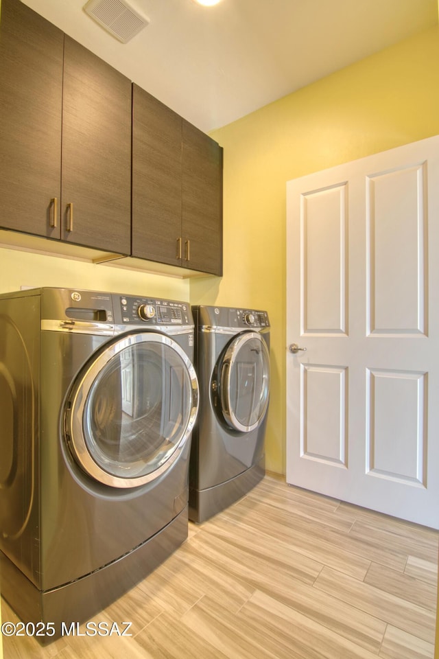 clothes washing area featuring separate washer and dryer and cabinets