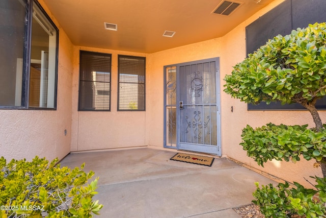 entrance to property featuring visible vents, a patio, and stucco siding