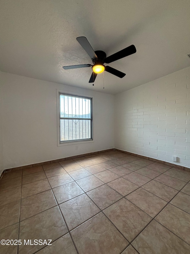 spare room featuring a ceiling fan, light tile patterned flooring, a textured ceiling, brick wall, and baseboards