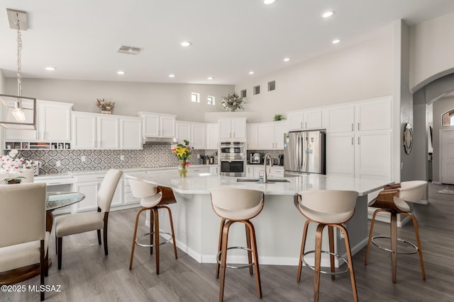 kitchen with an island with sink, white cabinetry, sink, hanging light fixtures, and stainless steel appliances