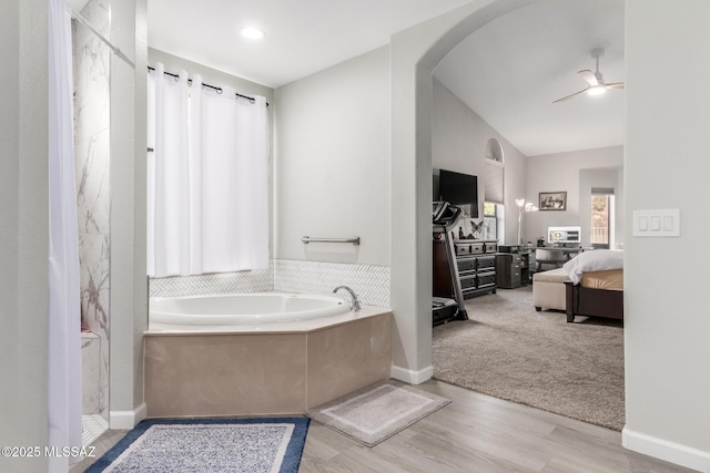 bathroom with hardwood / wood-style flooring, ceiling fan, a bathing tub, and vaulted ceiling