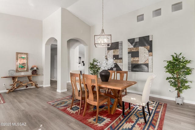 dining space featuring wood-type flooring, high vaulted ceiling, and a chandelier