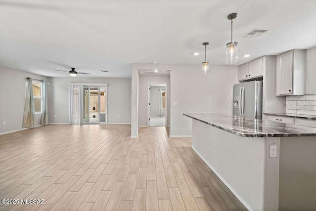 kitchen with dark stone countertops, hanging light fixtures, light hardwood / wood-style flooring, and stainless steel refrigerator with ice dispenser