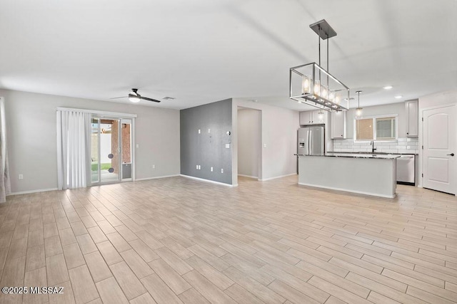 unfurnished living room with sink, light hardwood / wood-style floors, and ceiling fan with notable chandelier