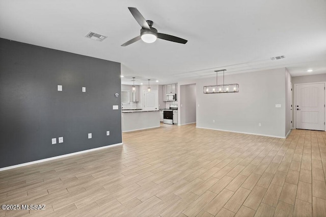 unfurnished living room featuring ceiling fan with notable chandelier and light wood-type flooring