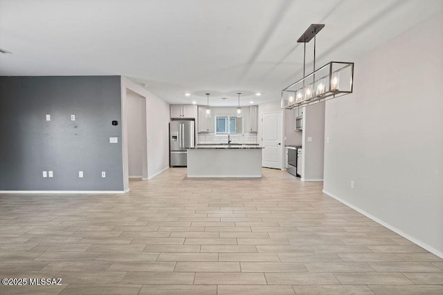 kitchen with a kitchen island, appliances with stainless steel finishes, backsplash, hanging light fixtures, and light hardwood / wood-style floors