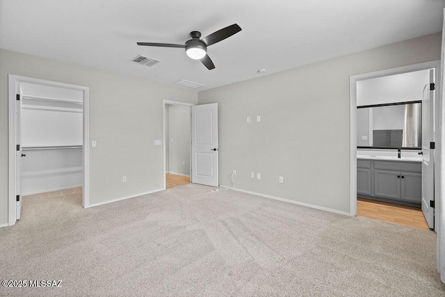 unfurnished bedroom with ceiling fan, a walk in closet, light colored carpet, and ensuite bath