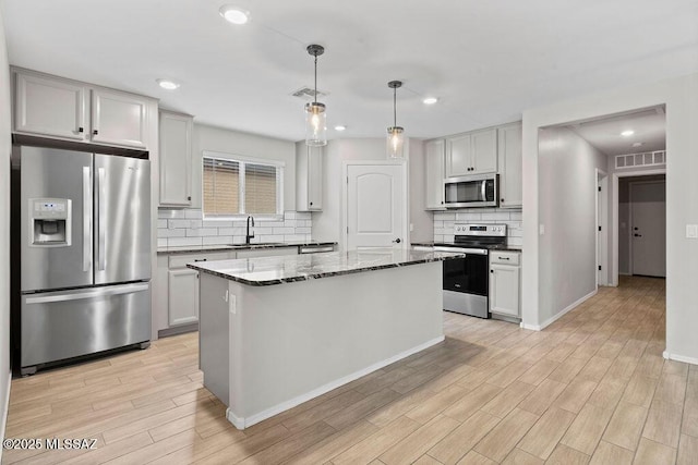 kitchen with sink, appliances with stainless steel finishes, a center island, light stone countertops, and decorative light fixtures