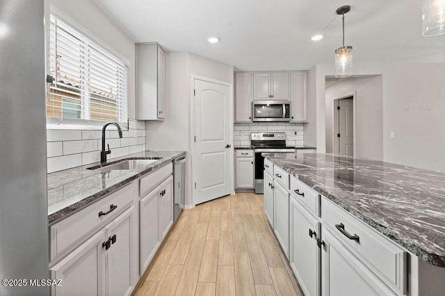 kitchen featuring appliances with stainless steel finishes, sink, dark stone countertops, and decorative light fixtures