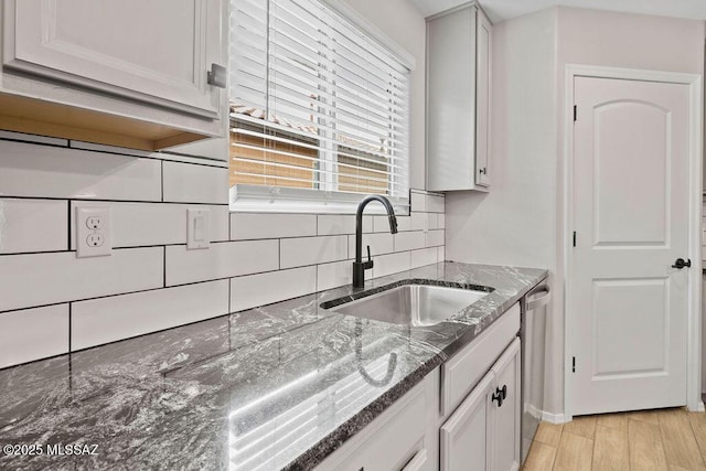 kitchen featuring white cabinets, stainless steel dishwasher, sink, and dark stone countertops