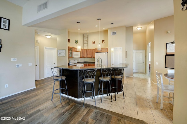 kitchen with a kitchen bar, decorative light fixtures, light wood-type flooring, a towering ceiling, and white appliances