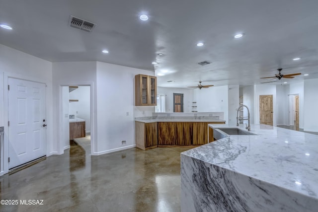 kitchen featuring concrete flooring, ceiling fan, sink, and light stone counters